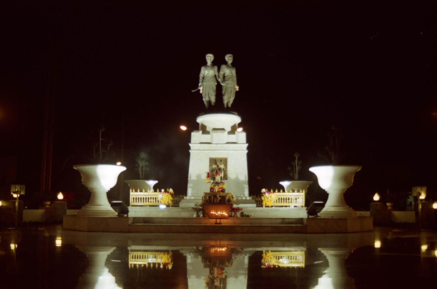 The Heroines' Monument: two bronze statues of Thao Thep Kasattri and Thao Sri Sunthon standing back to back on a tall white plinth, holding swords raised high, photographed at night with floodlights.