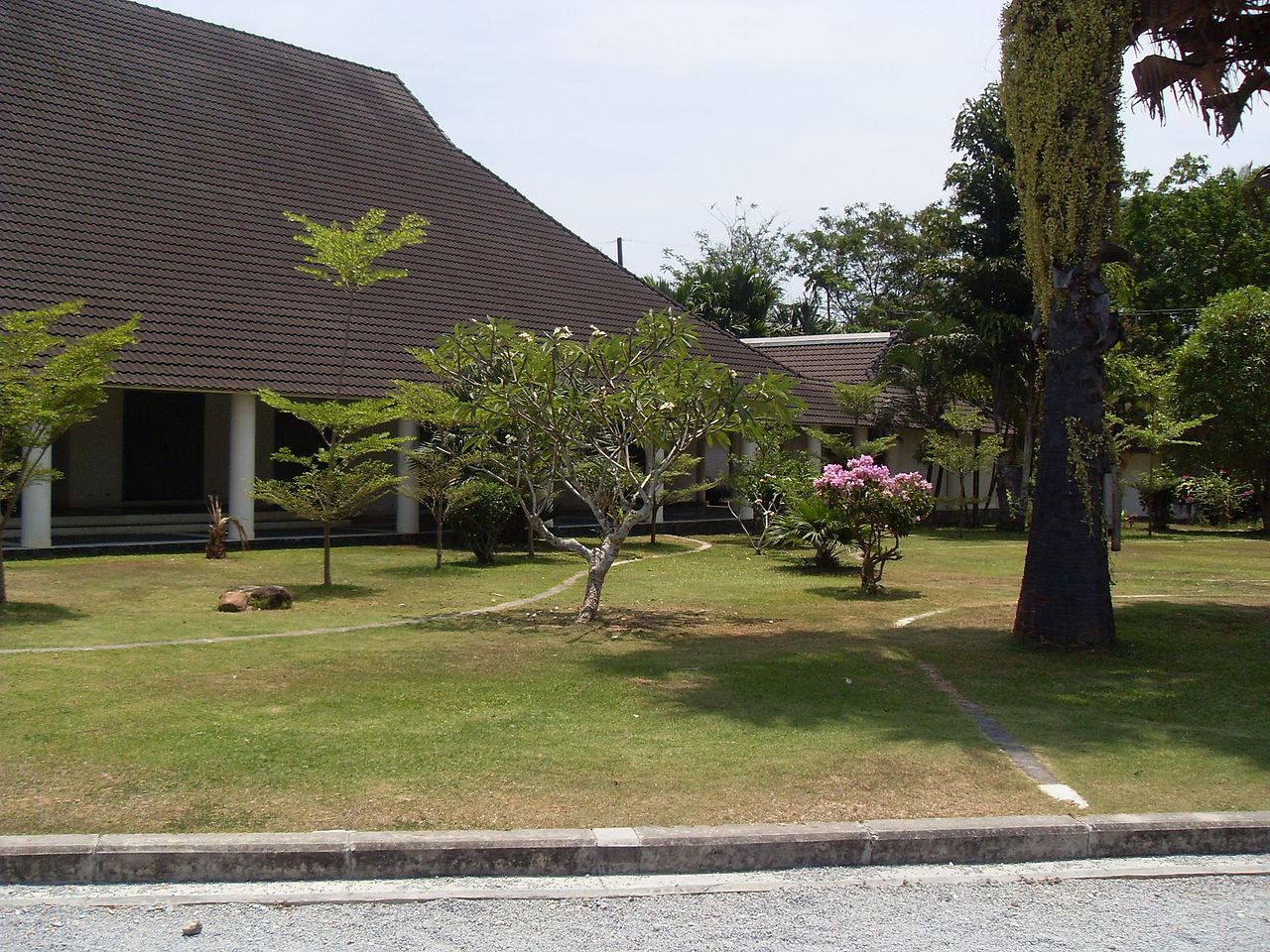 The Thalang National Museum, a low cream-coloured building with traditional Thai roofs, photographed in daylight with palm trees nearby.